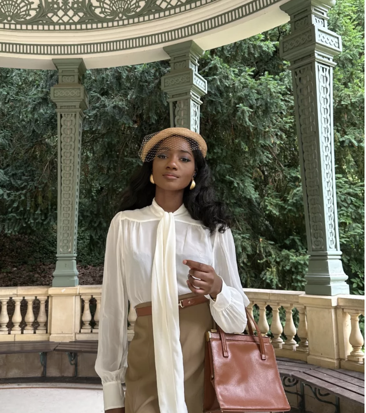 Dress like a lady and dress more feminine. Black woman wearing a hat, pearl earrings, white pussy blouse and brown skirt with a brown bag